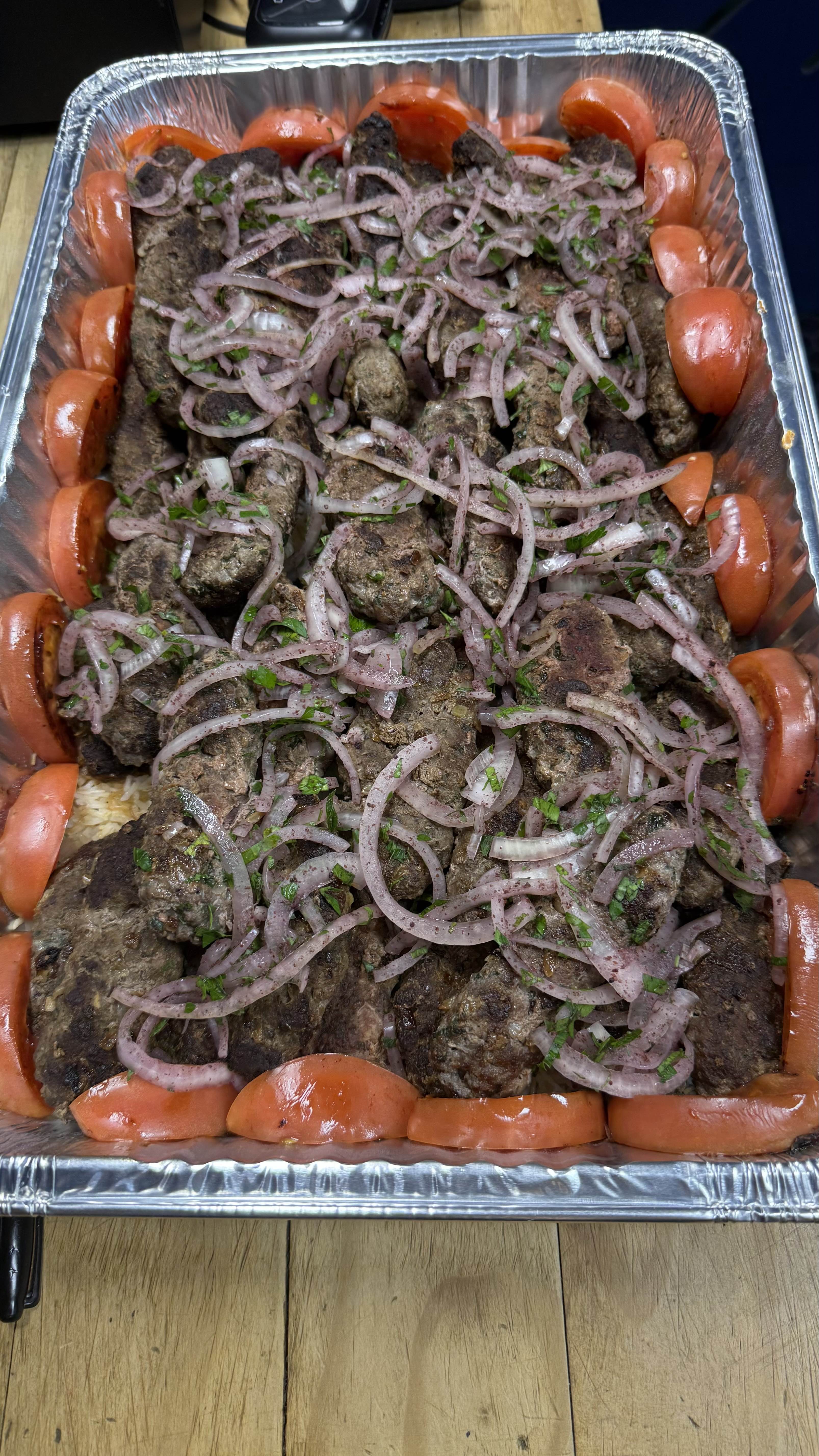 Kafta with sumac onions and tomatoes in a catering tray